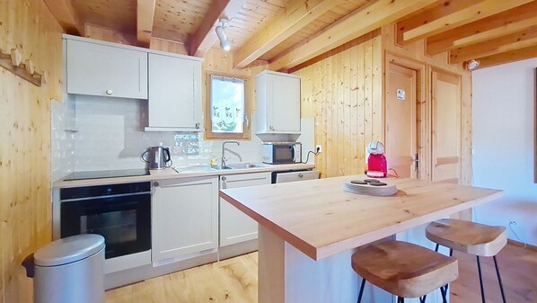 A wooden cabin interior with a kitchen area, including a stove, sink, and bar stools.