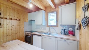 A compact kitchen with wooden walls, a window, and basic amenities like a sink, stove, and cabinets.