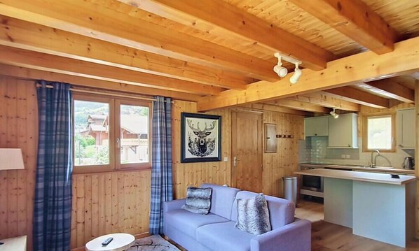 L'intérieur d'un chalet en bois, avec un canapé, un coin repas et une cuisine.