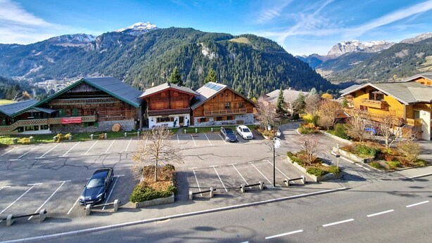 A mountain lodge with a parking lot, wooden cabins, and a view of snow-capped mountains. - Alpenlake AP139 VIEW & NATURE  6 Pers. (Châtel)