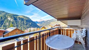 A balcony with a table and chairs, overlooking a mountainous landscape with wooden buildings. - Alpenlake AP139 VIEW & NATURE  6 Pers. (Châtel)