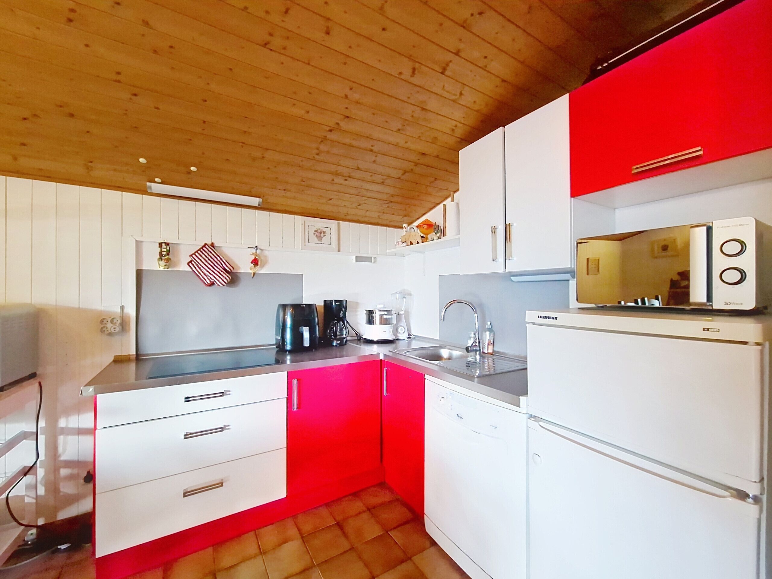 A compact kitchen with white cabinets, a red accent wall, a microwave, and a sink.