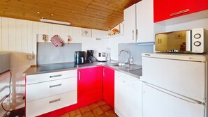 A compact kitchen with white cabinets, a red accent wall, a microwave, and a sink. - Alpenlake AP139 VIEW & NATURE  6 Pers. (Châtel)