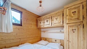 Una habitación de madera con una cama, armarios con detalles de corazones y una ventana con cortinas.