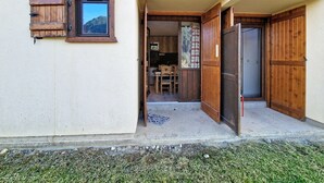 Un edificio rústico con un balcón de madera, un ventanal pequeño y una puerta que da a un espacio interior con una mesa y sillas.