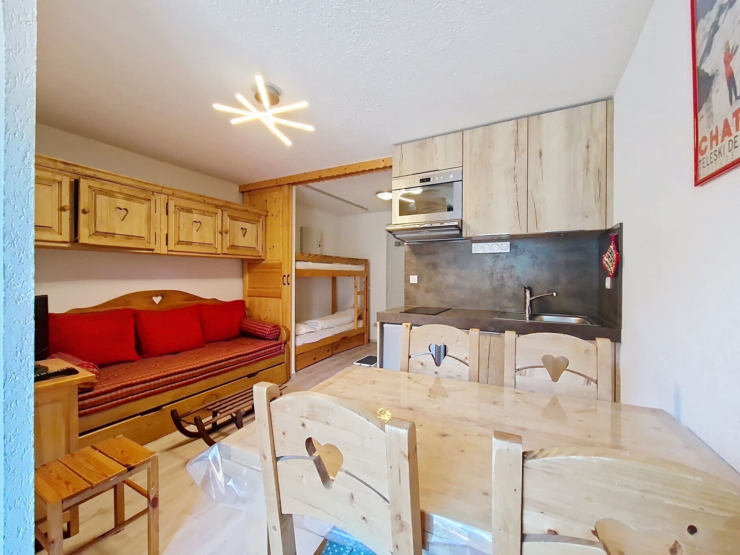 A compact kitchen with wooden cabinets, a built-in oven, and a sink. There is a dining table with chairs and a bench with red cushions.
