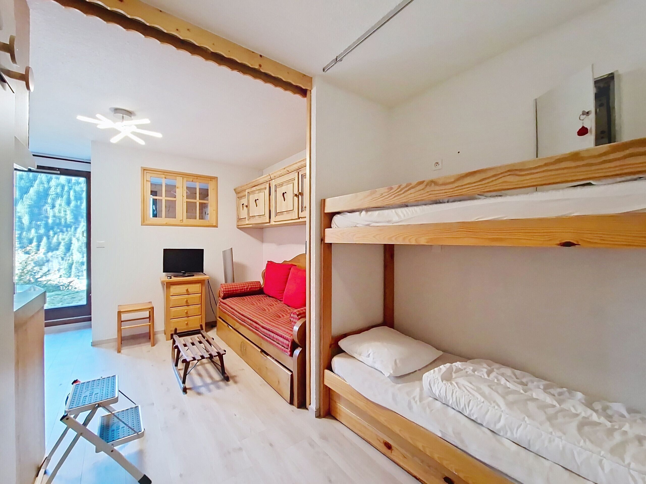 Una habitación con literas, un escritorio con silla, un televisor y una ventana con vista a árboles.