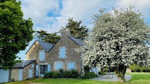 A stone house with a traditional design, a gravel driveway, and a flowering tree in the foreground. - Grande Maison de Vacances et WE Près de Dinan (Trévron)