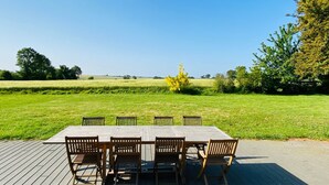 A wooden deck with a table and chairs, overlooking a grassy field with trees and a clear sky. - Grande Maison de Vacances et WE Près de Dinan (Trévron)