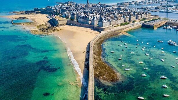 An aerial view of a coastal city with a prominent castle, a sandy beach, and a marina with numerous boats. - Grande Maison de Vacances et WE Près de Dinan (Trévron)