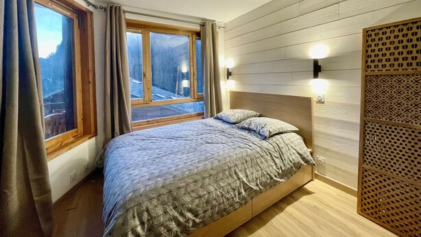 A bedroom with a bed, two windows, a wooden headboard, and a wall-mounted light fixture. - VAL PIERRE VPS8 CENTER & MODERN 4 Pers. (Châtel)