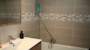 A bathroom with a white sink, a mirror, a shower with a handheld showerhead, and tiled walls with a geometric pattern. - VAL PIERRE VPS8 CENTER & MODERN 4 Pers. (Châtel)