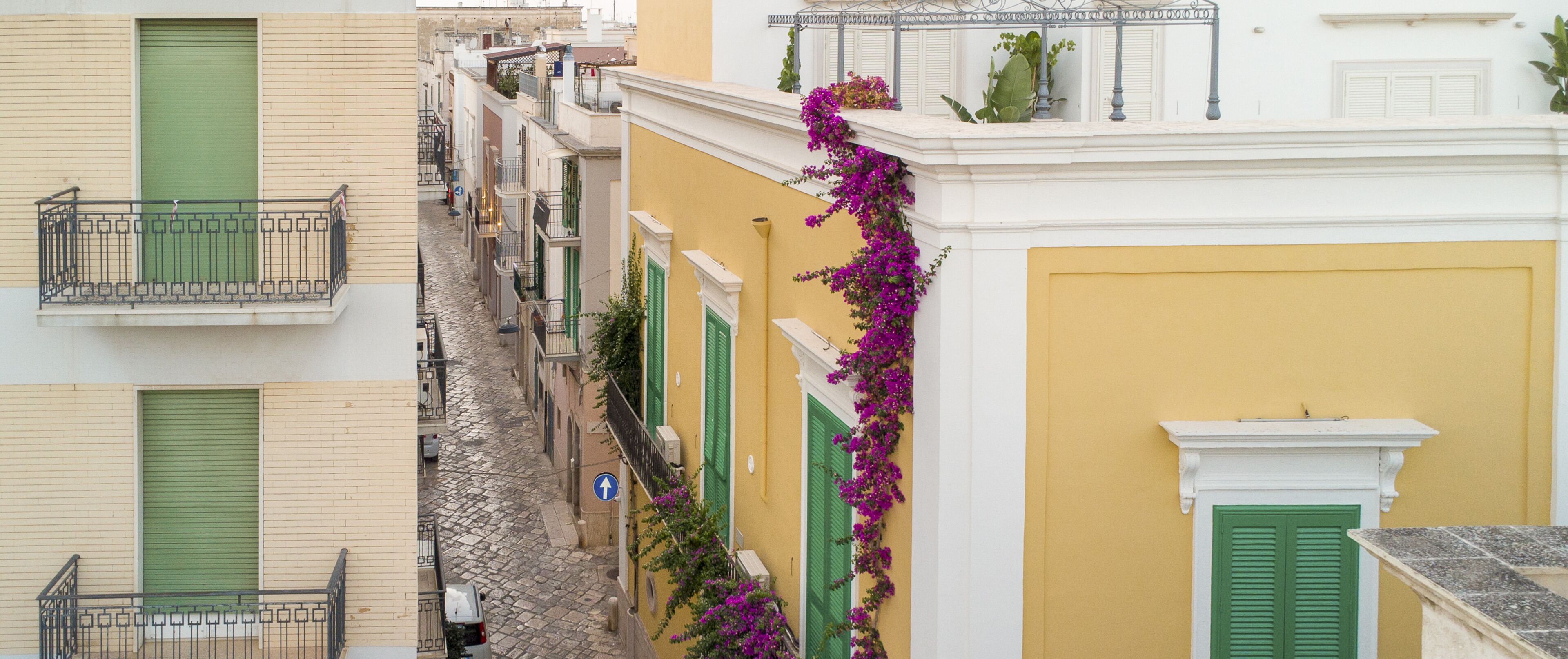 A narrow street with buildings featuring balconies and green shutters.