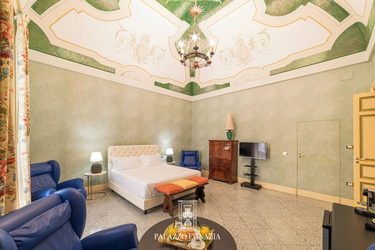 Een hotelkamer met een bed, twee blauwe fauteuils, een tafeltje met een schaal fruit, een televisie en een kast.