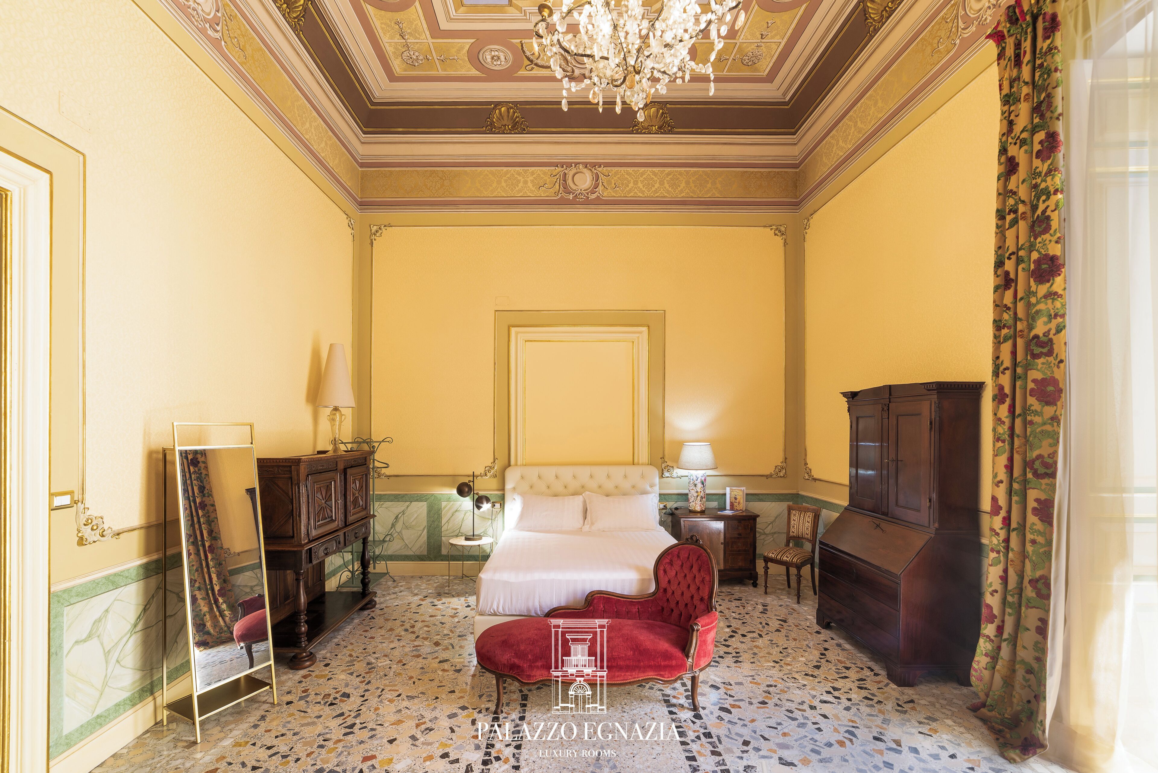 Un dormitorio lujoso con una cama grande, un sillón rojo, un armario de madera y un espejo.