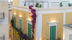 Een meerhoog gebouw met groene luiken, een balkon met ijzeren spijlen en een trap versierd met paarse bloemen.