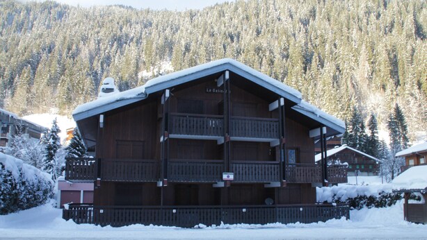 A multi-story wooden building with balconies, surrounded by snow-covered trees and a mountain in the background. - Gelinote GL3 TELECABINE & MOUNTAIN 4 Pers. (Châtel)