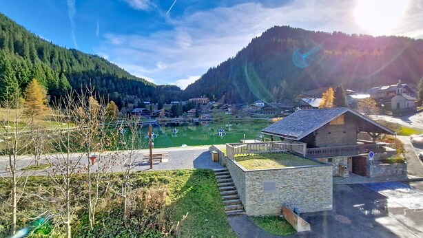 A mountain village with a stone building, a green field, and a lake. - Alpenlake AP120 VIEW & NATURE 5 pers. (Châtel)