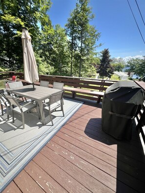 Eine Holzterrasse mit Tisch und Stühlen, einem überdachten Grill und einer Bank.