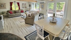 A spacious living area with a wooden floor, a dining table with chairs, a sofa, and a coffee table. - SEBAGO LAKE BEACH ACCESS (Sebago)