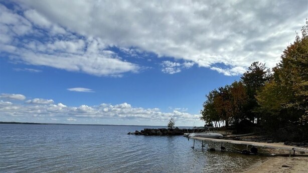 A beach with clear water, a sandy shore, and a dock extending into the water. - SEBAGO LAKE BEACH ACCESS (Sebago)
