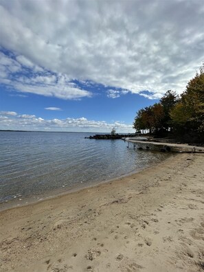 A beach with clear water, a sandy shore, and a dock extending into the water.