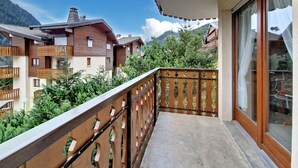 Un balcon doté d’une balustrade en bois, d’une porte vitrée et offrant une vue sur les bâtiments et les montagnes environnants.