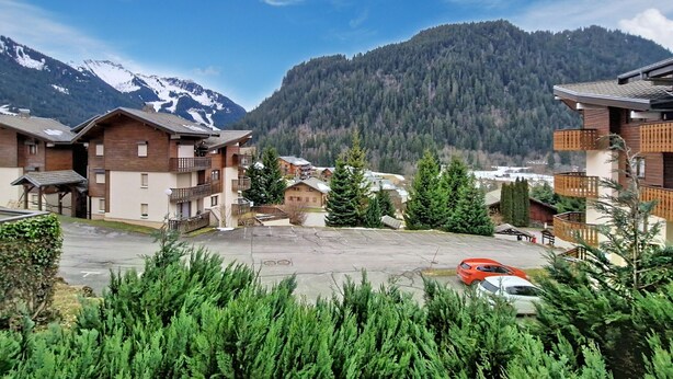 Un village de montagne avec des bâtiments en bois, un espace de stationnement et une vue sur des montagnes enneigées.