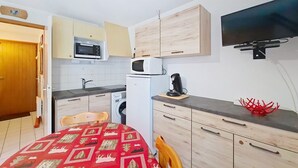 Une cuisine compacte équipée d’un four à micro-ondes, d’une machine à café et d’un téléviseur fixé au mur.