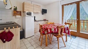 Une cuisine compacte équipée d’un four à micro-ondes, d’une cuisinière et d’un réfrigérateur. On y trouve une table à manger avec des chaises, et une vue sur un balcon agrémenté d’une balustrade.