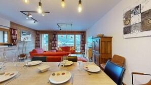 Una sala de estar acogedora con un sofá rojo, una mesa de comedor con platos y vasos, y vista a un paisaje nevado a través de amplios ventanales.