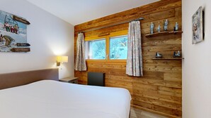 Habitación de hotel con pared de madera, cama, mesita de noche, lámpara, ventana con cortinas y decoración en la pared.