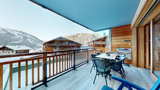 Una terraza de madera con una mesa y sillas, con vistas a un paisaje montañoso nevado.