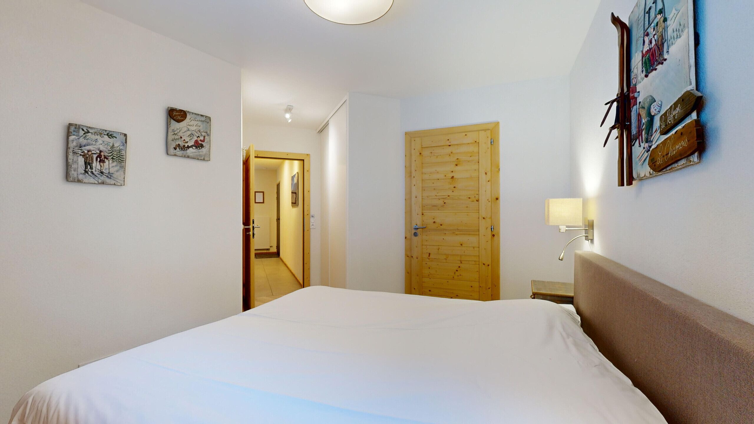 Een slaapkamer met een groot bed, een houten deur en een kunstwerk aan de muur.