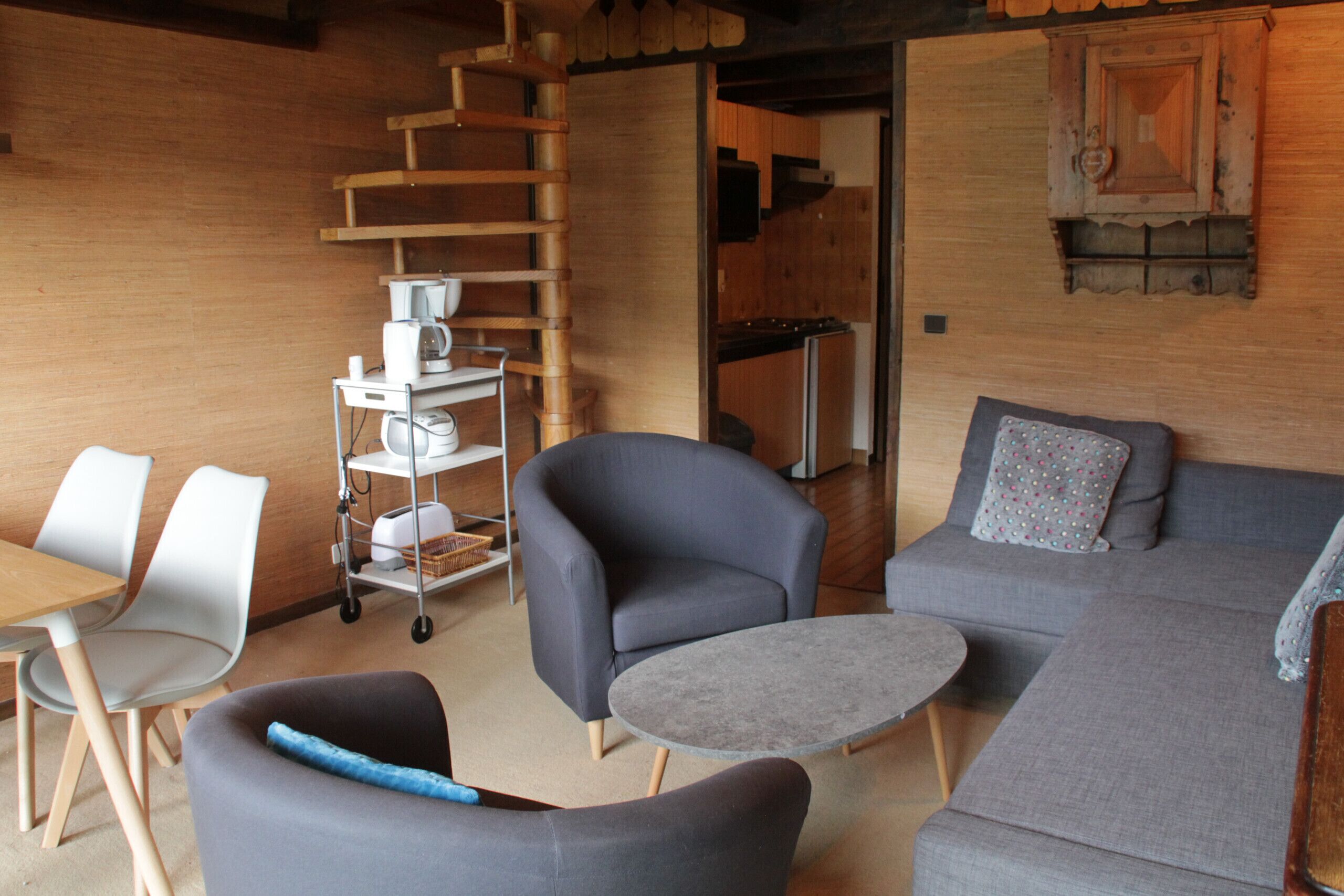 A modern living room with a grey sofa, two armchairs, a small round table, and a wooden ladder against the wall.