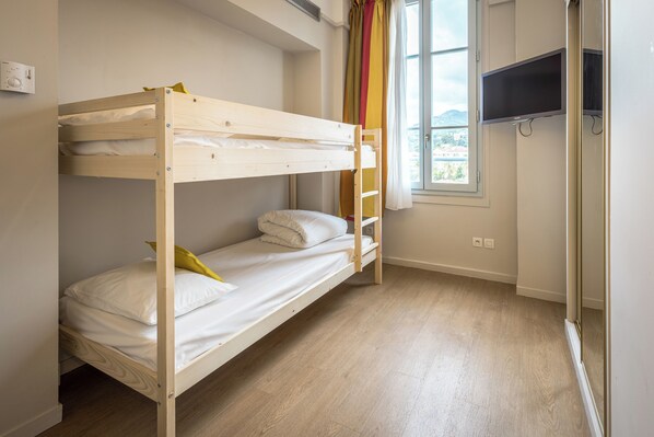 A bunk bed room with a window, a TV mounted on the wall, and a wooden floor. - L'Orangeraie Hotel by Miléade (Menton)