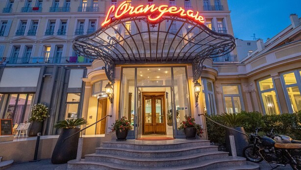 A hotel entrance with a prominent neon sign, a grand staircase, and a classic architectural style. - L'Orangeraie Hotel by Miléade (Menton)
