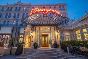 A hotel entrance with a prominent neon sign, a grand staircase, and a classic architectural style. - L'Orangeraie Hotel by Miléade (Menton)