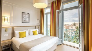 A hotel room with a large bed, a bedside table, a lamp, a framed picture on the wall, and a balcony with a view of the city. - L'Orangeraie Hotel by Miléade (Menton)