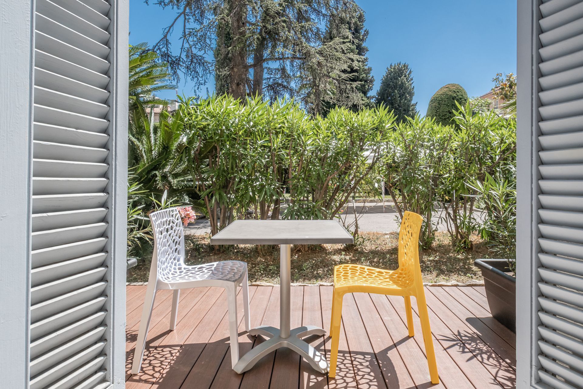 Un patio exterior con una mesa y dos sillas, rodeado de follaje y árboles.