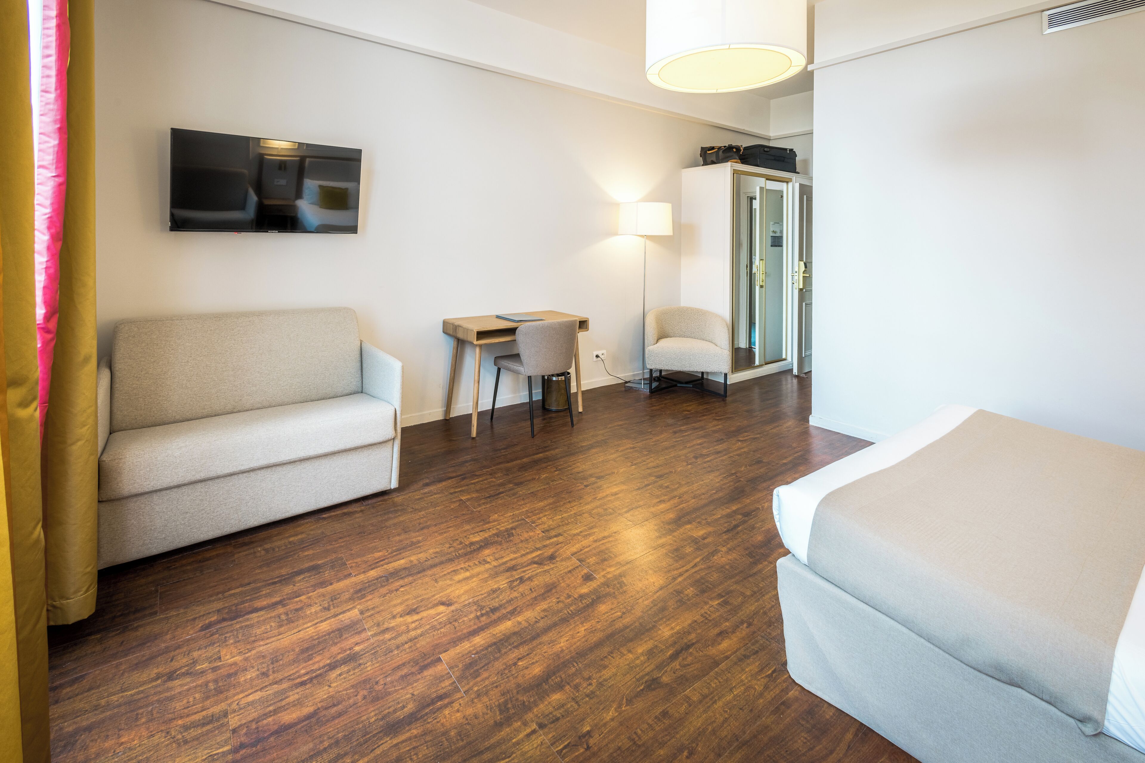 Hotelkamer met een bank, een klein bureau, een stoel, een bed en een aan de muur bevestigde televisie.