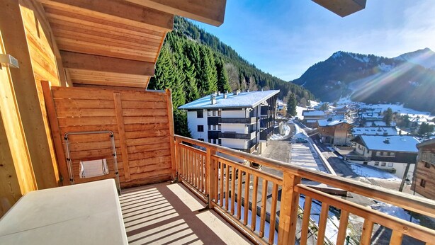 A wooden balcony with a view of a snowy village and mountains.