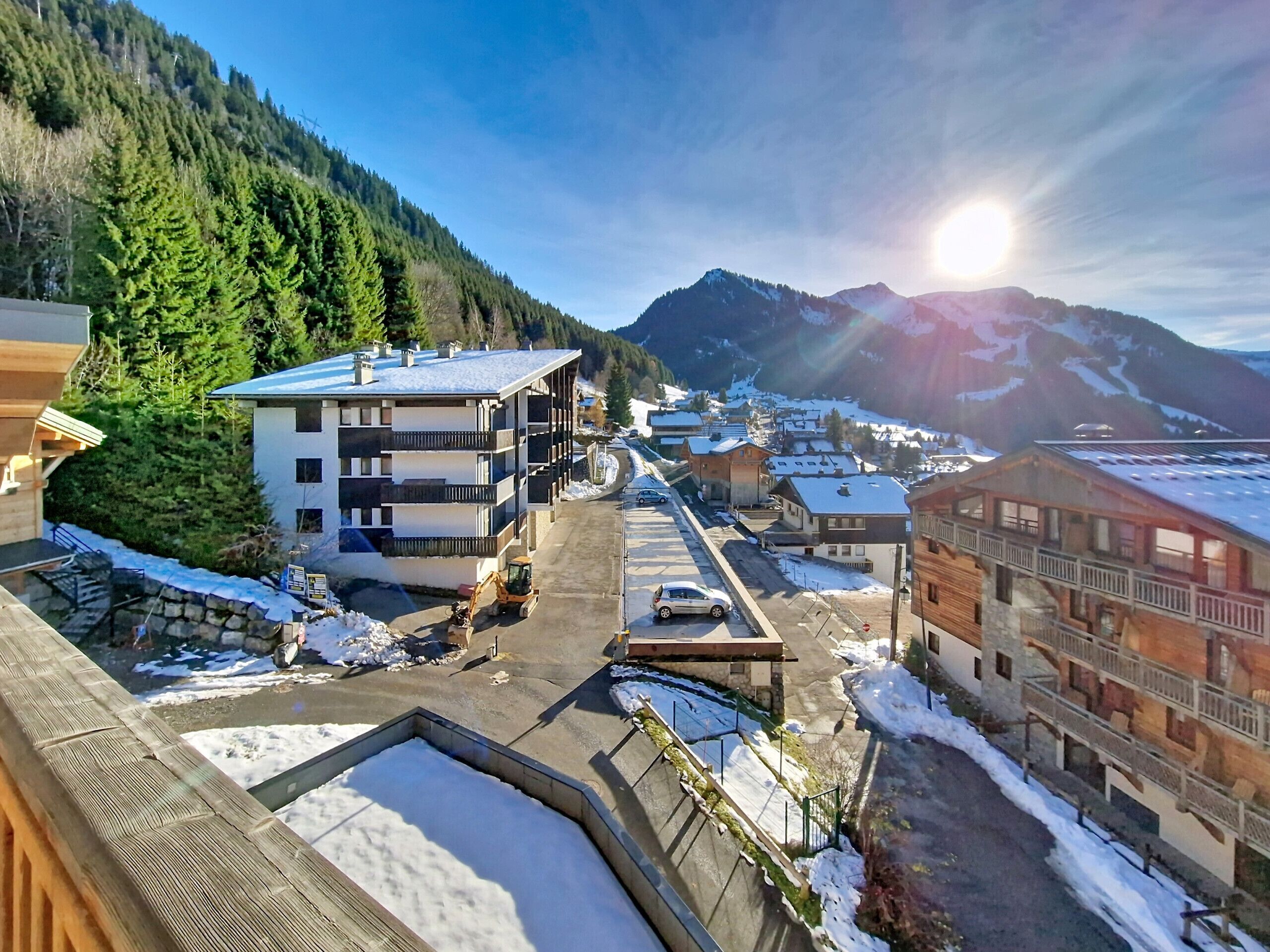 A modern multi-story building with balconies, a parking area, and a view of snow-covered mountains.