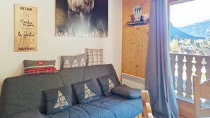 A cozy living room with a dark grey sofa, decorative pillows, a wooden wall, a large deer painting, and a view of a mountainous landscape through a window. - Forsythia FA18 FAMILY 1& NATURE 4 Pers. (Châtel)