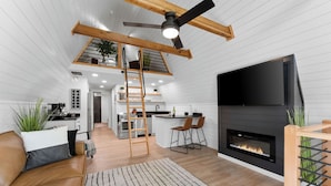 Una sala de estar moderna con chimenea, televisión y cocina al fondo.
