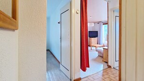Un pasillo con piso de madera, una cortina roja y un televisor en una habitación.