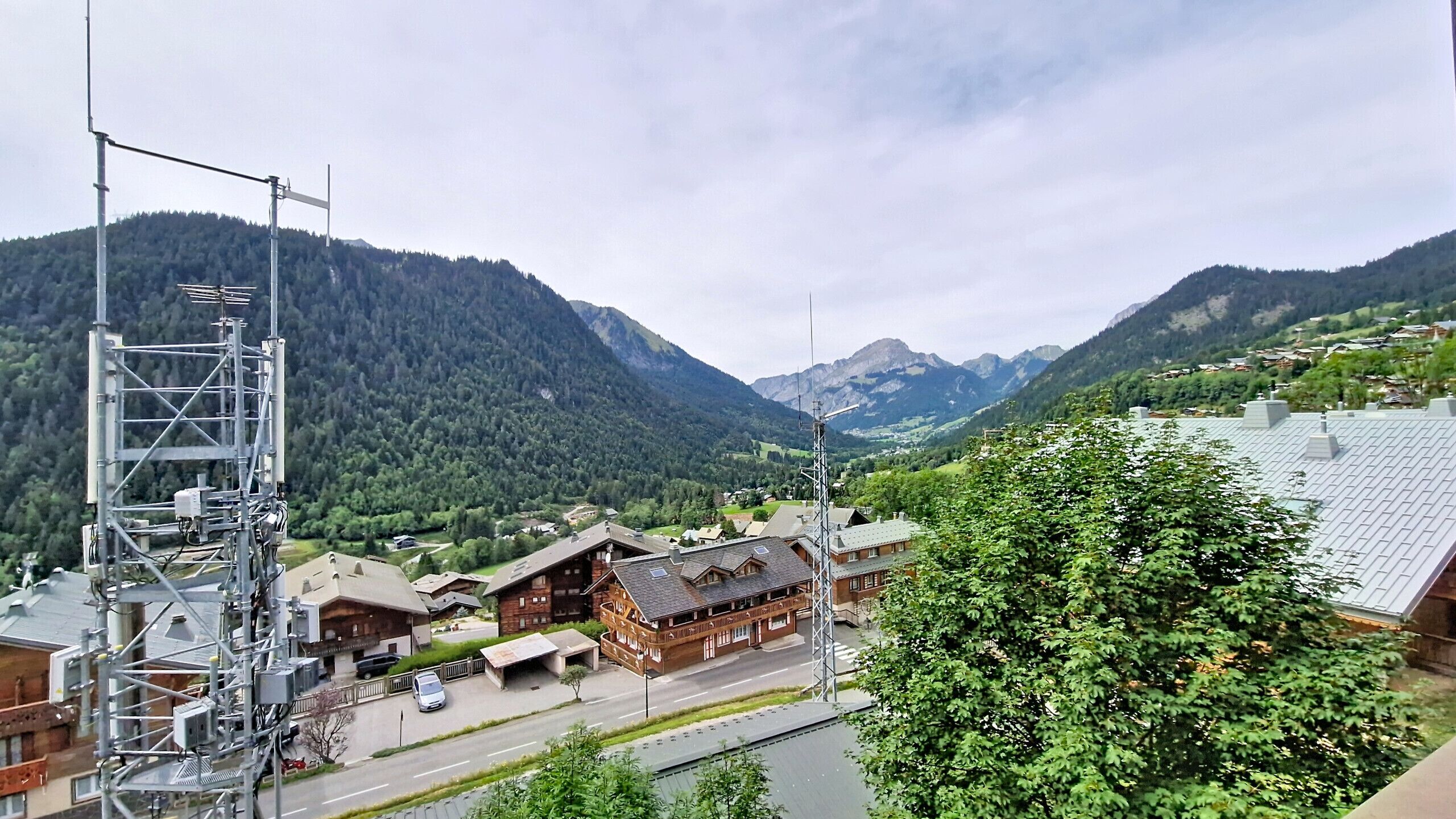 Un paisaje montañoso con un edificio de madera, una carretera y una torre de servicios.