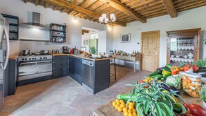 A kitchen with a central island, wooden beams, and a variety of fruits and vegetables on the counter. - Villa a Casa di Giovanni 12, Emma Villas (Acquapendente)