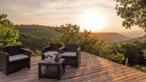 A wooden deck with wicker furniture and a table set for two, overlooking a forested valley at sunset. - Villa a Casa di Giovanni 12, Emma Villas (Acquapendente)