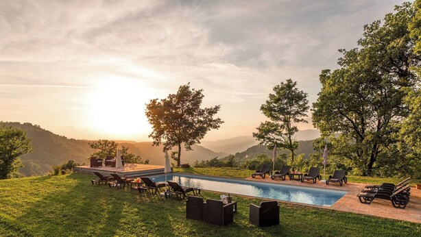 A poolside area with lounge chairs and umbrellas, surrounded by trees and a view of distant hills. - Villa a Casa di Giovanni 12, Emma Villas (Acquapendente)